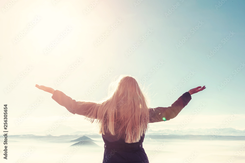 A young blond woman with raised hands enjoys the fresh mountain air and beautiful views of the mountains. A young blond woman with raised hands enjoys the fresh mountain air and beautiful views of the mountains.