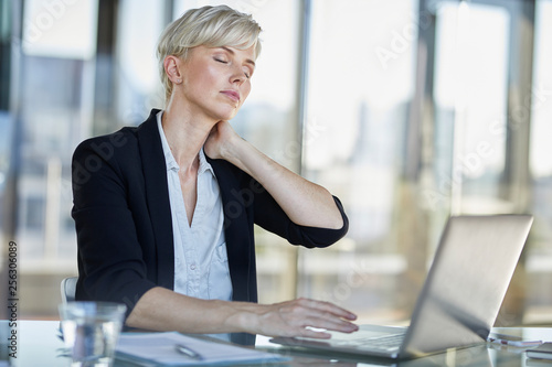 Exhausted businesswoman sitting at desk in office with closed eyes photo