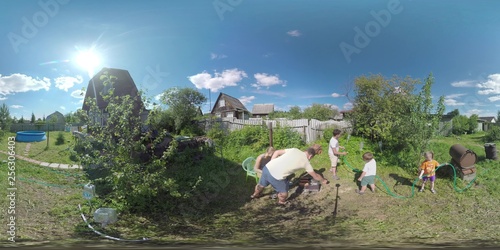 360 VR video. Parents and children in the countryside. Mother and father making sausage barbecue while kids watering plants in the house yard. Ruza in Moscow region, Russia photo