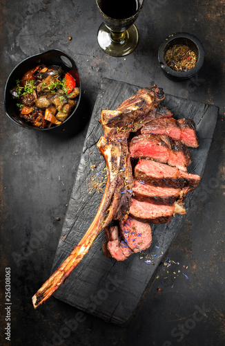 Traditional barbecue dry aged wagyu tomahawk steak sliced with ratatouille as top view on a rustic carbonized wooden board