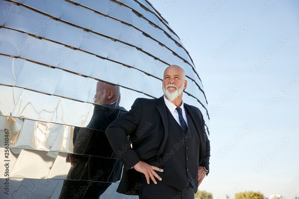 Elegant businessman standing in the city, in front of mirror facade, with hands on hips Elegant businessman standing in the city, in front of mirror facade, with hands on hips