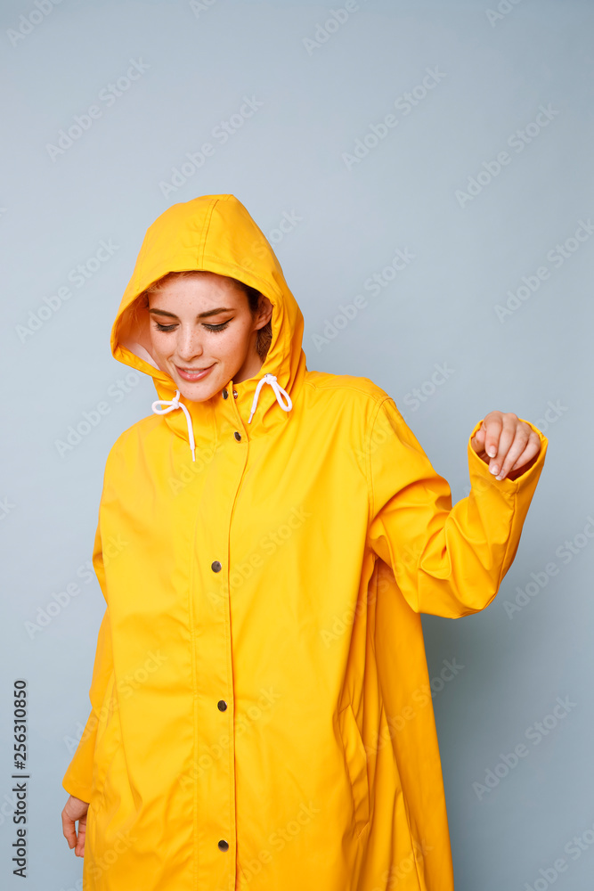 Smiling young woman wearing yellow rain coat in front of blue background dancing Smiling young woman wearing yellow rain coat in front of blue background dancing