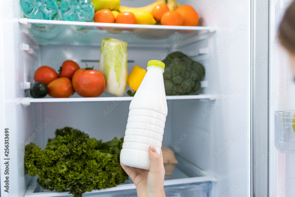Woman standing in front of fridge and taking milk. Fridge full of groceries. Woman standing in front of fridge and taking milk. Fridge full of groceries.