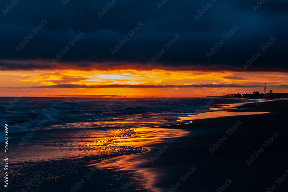Fototapeta premium Beautiful sunset at the edge of the sea. The sky and the sand are covered with golden reflections.