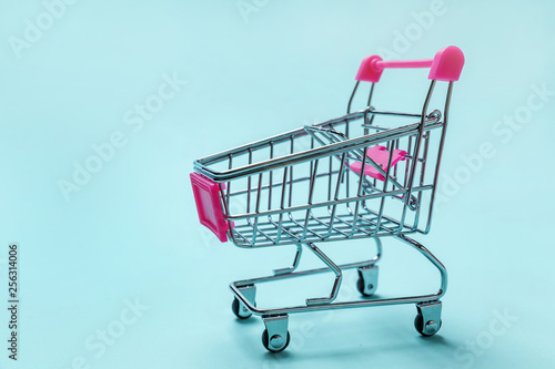 Sale buy mall market shop consumer concept. Small supermarket grocery push cart for shopping toy with wheels isolated on blue pastel colorful paper trendy background. Copy space