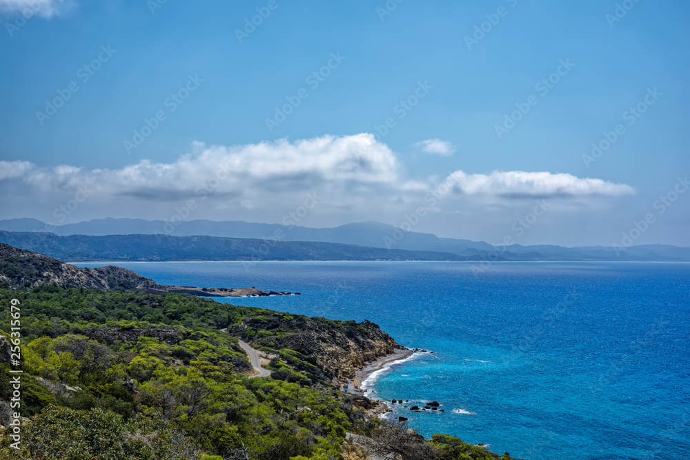 Panoramic view of the coastal rocks of the Mediterranean Sea, overgrown with green forest in the early summer morning. Rhodes island, Greece.