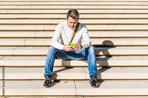 Casual businessman sitting on stairs, reading messages on his smartphone