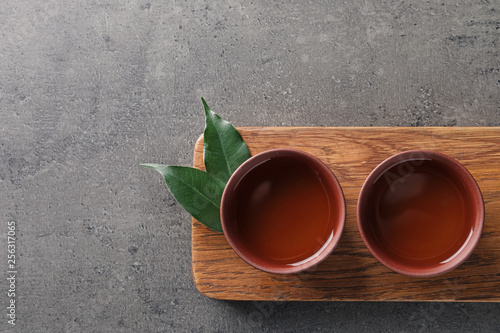 Board with cups of freshly brewed oolong tea on grey background, top view with space for text