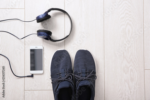 Flat lay composition with sneakers, headphones and mobile phone on wooden background. Space for text