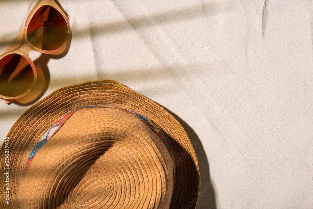 Obraz premium Hat and sunglasses on beach sand, top view. Space for text