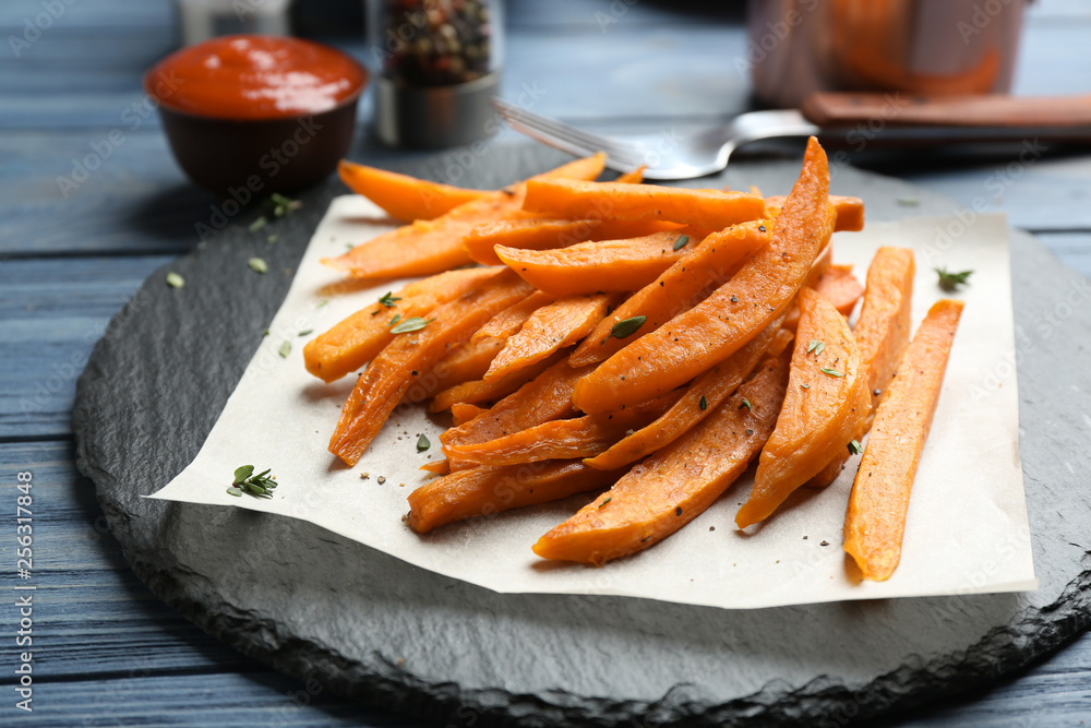 Slate plate with tasty sweet potato fries on wooden table Slate plate with tasty sweet potato fries on wooden table