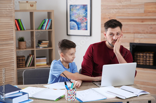 Dad helping his son with difficult homework assignment in room, space for text
