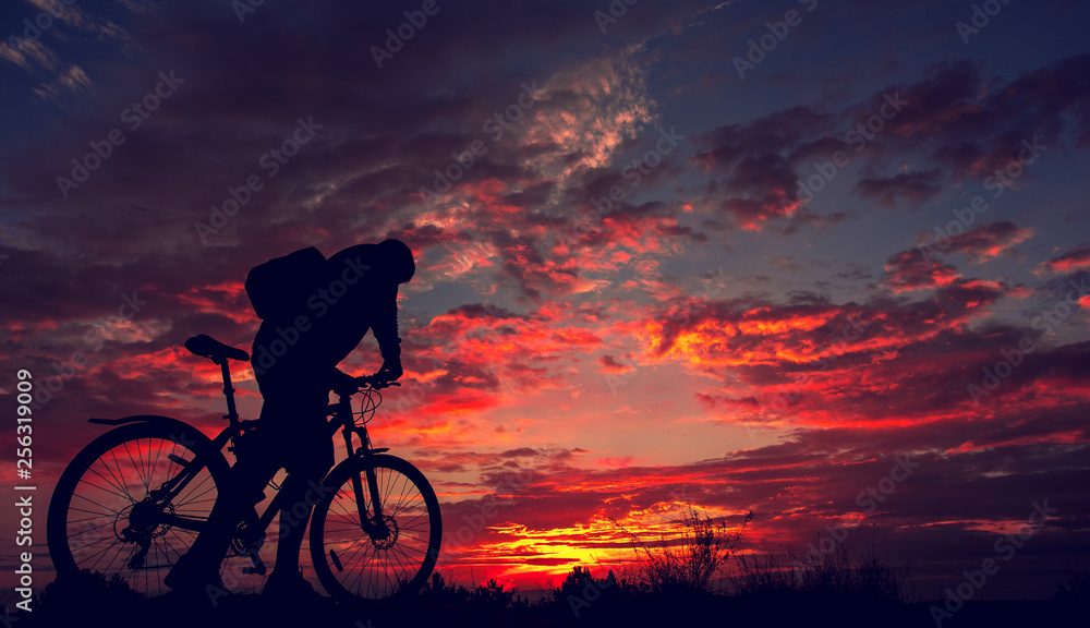 Obraz premium cyclist with a bicycle, in the background fiery sunset.