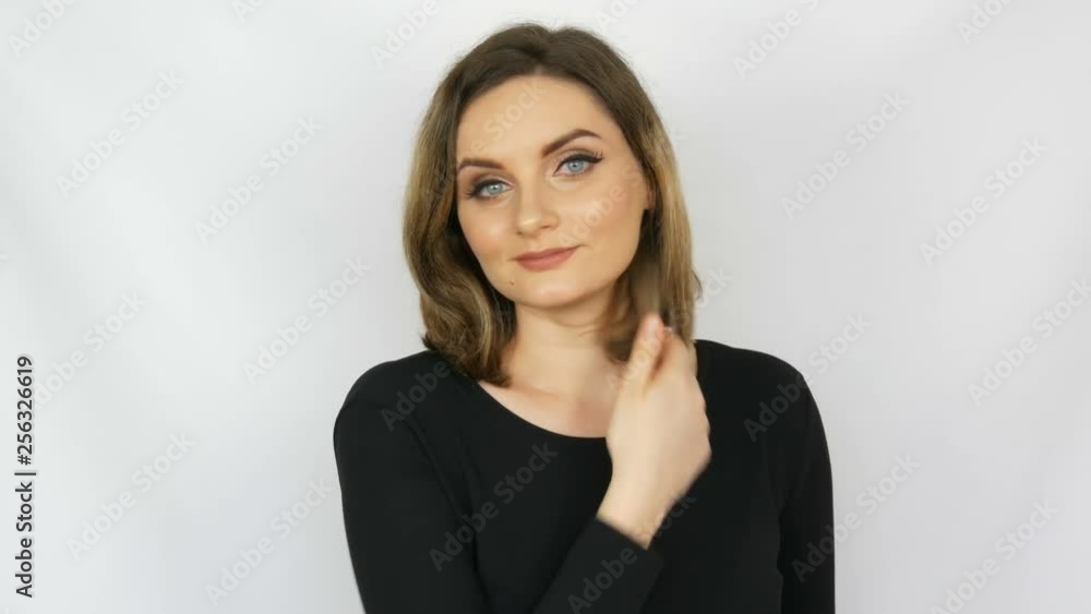 Portrait of a beautiful young sexy elegant woman in a black dress who touches her hair, straightens her hair and looks into the camera while smiling on a white background Portrait of a beautiful young sexy elegant woman in a black dress who touches her hair, straightens her hair and looks into the camera while smiling on a white background