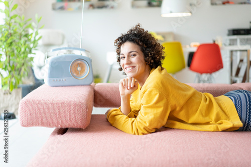 Portrait of happy woman lying on couch listening to music with portable radio at home photo