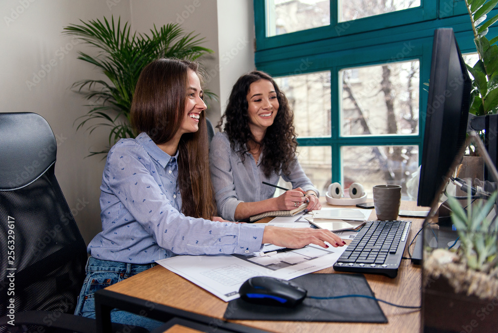 Two beautiful female designers or architects jointly solve work tasks while working in modern office near window. Creative people or advertising business concept. Two beautiful female designers or architects jointly solve work tasks while working in modern office near window. Creative people or advertising business concept.