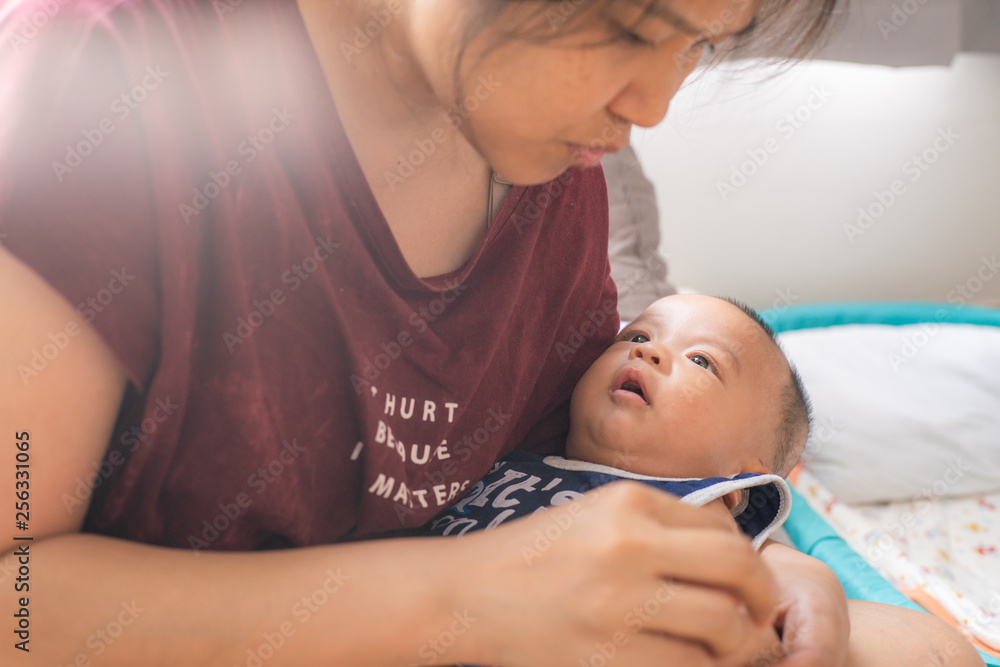 Fototapeta premium Asian women holding smiling infant boy in bedroom