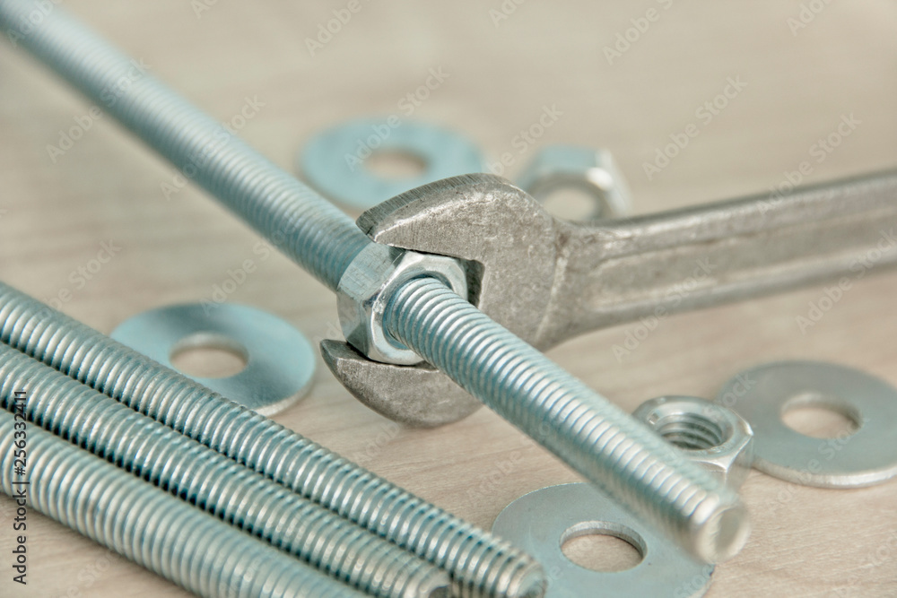 Metal Wrench Grip and Rotate Nut Around Metal Bolt Close-Up on Wooden Table Among Bolts, Studs, Nuts and Washers. Background. Metal Wrench Grip and Rotate Nut Around Metal Bolt Close-Up on Wooden Table Among Bolts, Studs, Nuts and Washers. Background.