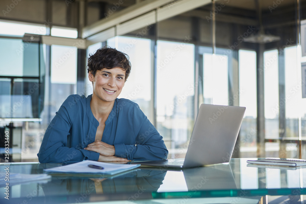 Portrait of confident businesswoman sitting at desk in office with laptop Portrait of confident businesswoman sitting at desk in office with laptop