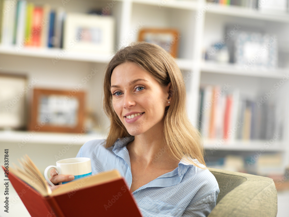 Smiling young woman relaxing at home with a hot drink and a book Smiling young woman relaxing at home with a hot drink and a book