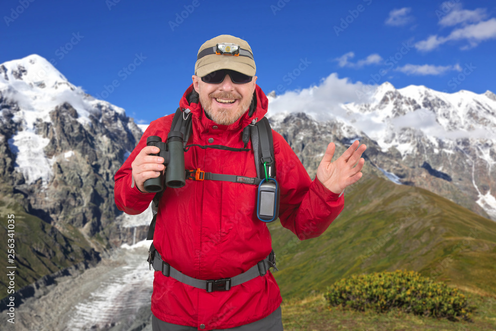 Happy man traveler with binoculars in hand on snow-capped mountains background