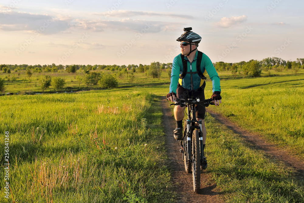 Obraz premium cyclist rides on the road in a field on a bright sunny day.