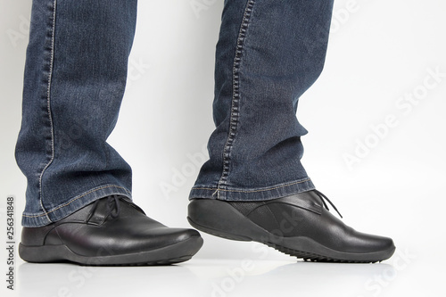 Men's legs in jeans and black classic shoes on white background