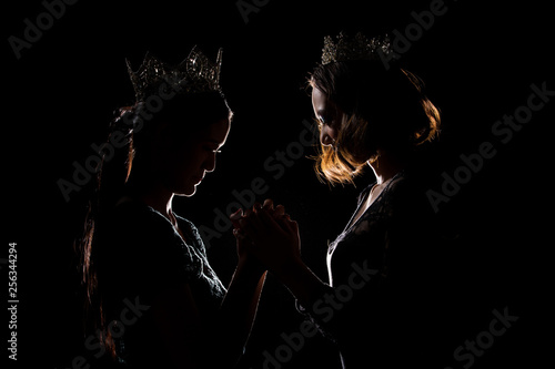 Two Silhouette Shadow Back Rim Light of Miss Pageant Beauty Queen Contest with Silver Diamond Crown hold pray together for final moment announce Winner prize, studio lighting dark black background © Jade