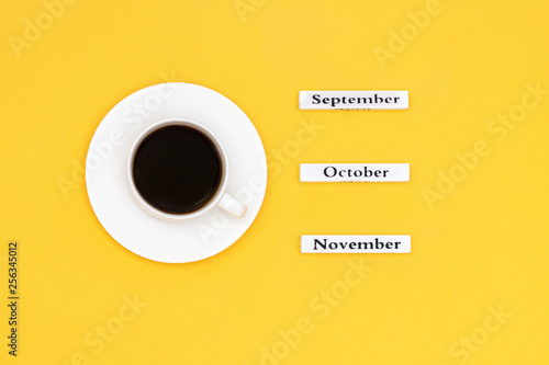 Wooden calendar autumn months September October November and Cup of black coffee aimed at November on yellow background. Concept Top view Flat Lay Copy space