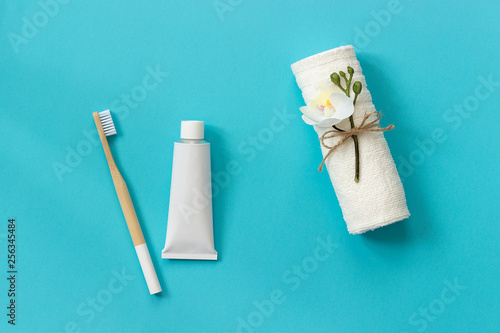 Natural eco-friendly bamboo brush, white towel and tube of toothpaste. Set for washing on paper blue background. Copy space for text or your design Top view Flat lay.