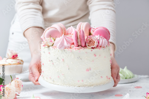 Confectioner puts a beautiful white cake with macarons and roses on a table