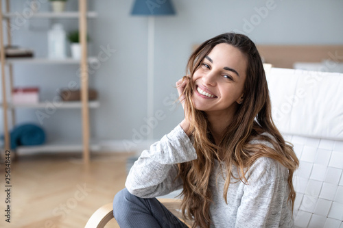 Smiling millennial girl sitting in a cozy chair at home.