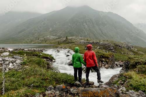 Couple of tourists standing by the mountain river on a foggy summer day in the rain