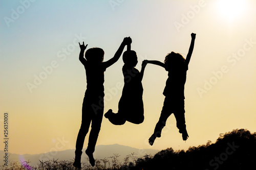 Silhouette of happy children jumping playing on mountain meadow at sunset time