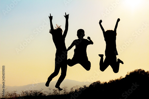 Silhouette of happy children jumping playing on mountain meadow at sunset time