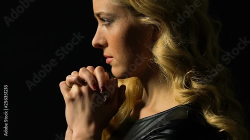 Girl praying isolated on black, light falling on face as sign of forgiveness