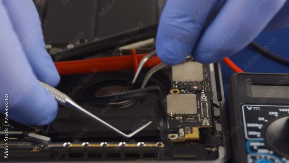 Engineer in blue gloves removes rubber from a laptop fan. Laptop in an aluminum case on a blue velvet background. Close-up Engineer in blue gloves removes rubber from a laptop fan. Laptop in an aluminum case on a blue velvet background. Close-up