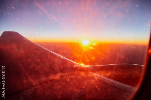 View of airplane wing, sunset and clouds through window of plane