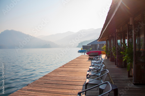 Soft sunlight in the morning and the terrace of floating home stay on the lake with chairs and table for tourists to relaxing time or time of freedom. The mountain view in background.