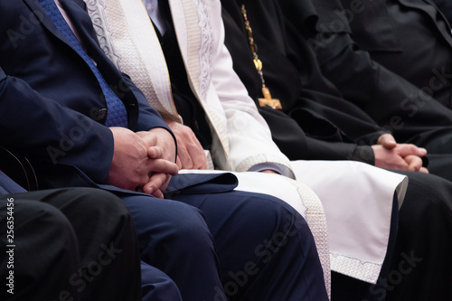A clerk in costume, a Muslim mullah in white and a priest in a black are sitting next to each. Blurred. Shallow depth of field. Conceptual background for design and news about religion and government.
