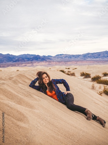 Girl with long hair in a plaid shirt sitting on a sand dune in Death Valley