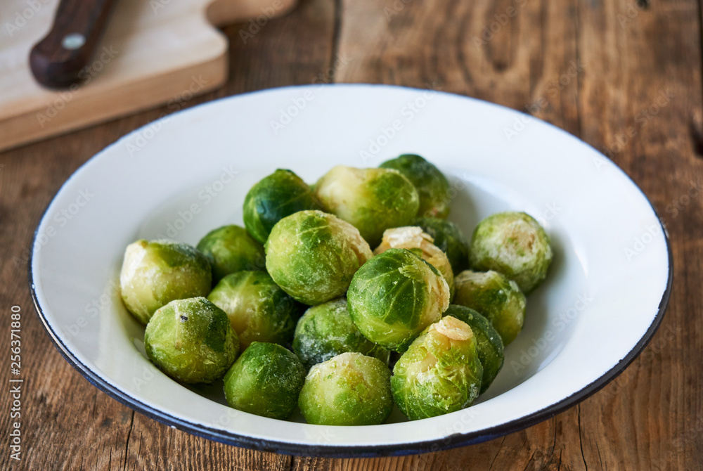 Frozen brussels sprouts in a white bowl on a wooden background Frozen brussels sprouts in a white bowl on a wooden background