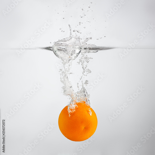 orange falls into the water scattering a lot of splashes and drops