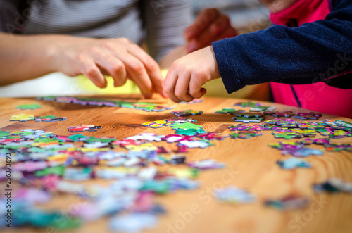 Hands of a little child and parent plying jigsaw puzzle game on a  table photo