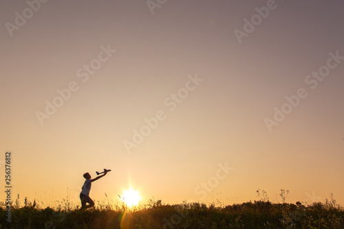 Young happy kid playing toy plane outside on summer sunset grassy hill. Horizontal color photography.