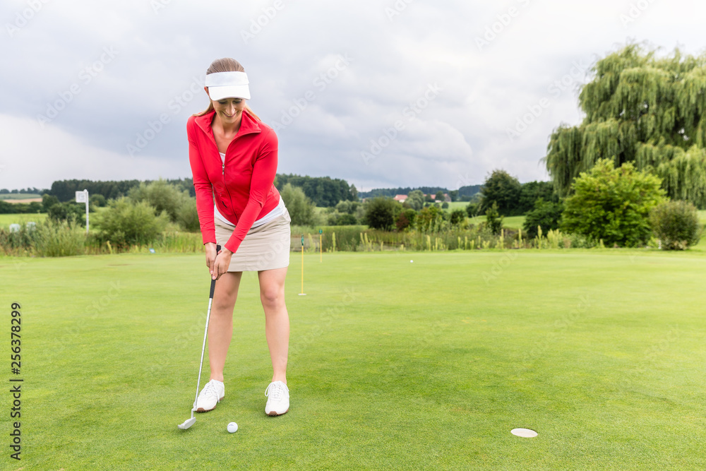 Female golfer putting ball in hole