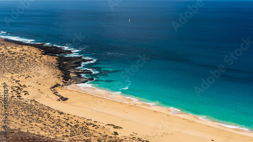 Exotic Las Conchas beach seen from above, a tropical paradise on La Graciosa Island, Canary, with turquoise sea waters in infinite shades of blue contrasting the white sand and volcanic black rocks.