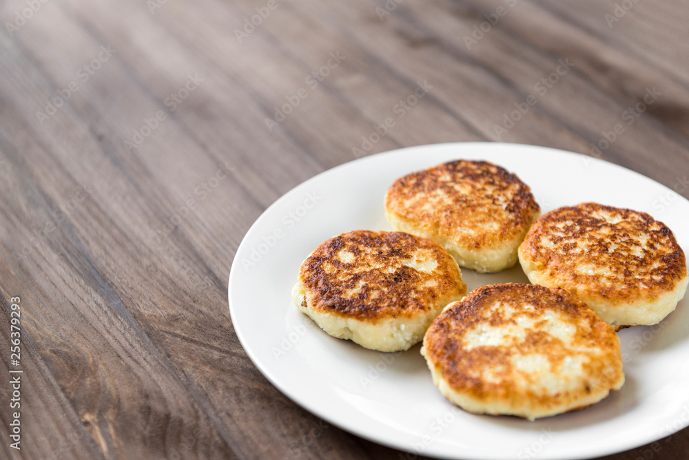 4 cheesecakes on a white plate on a wooden background, pancakes made of cottage cheese