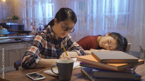 University young girl student sleeping sitting at wooden table in home kitchen at night by notebook computer. side view of asian hard working woman in glasses keep study concentrated stay up late