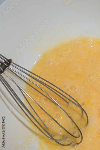 Whipping chicken eggs with a metal whisk in a mixing bowl
